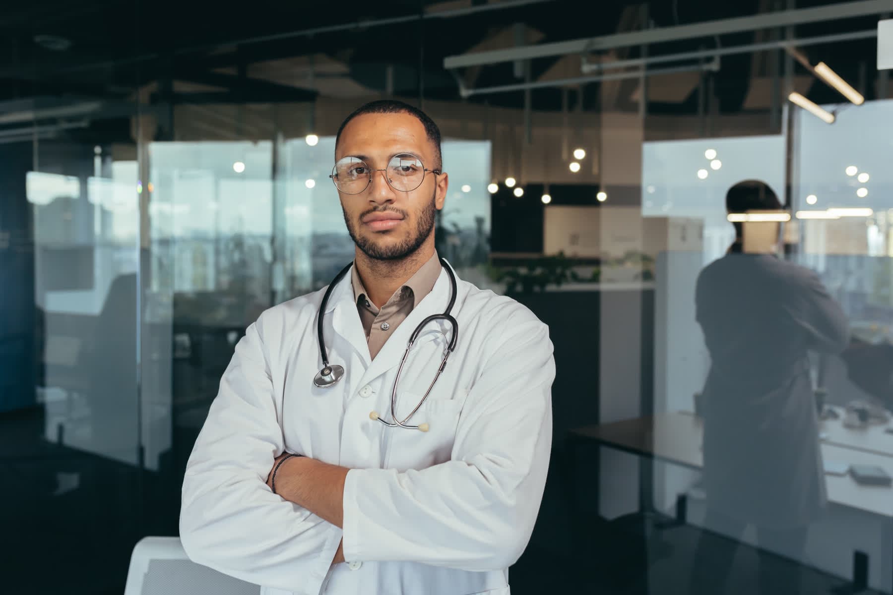 A specialist in a white coat, arms folded, photographed in a modern clinic