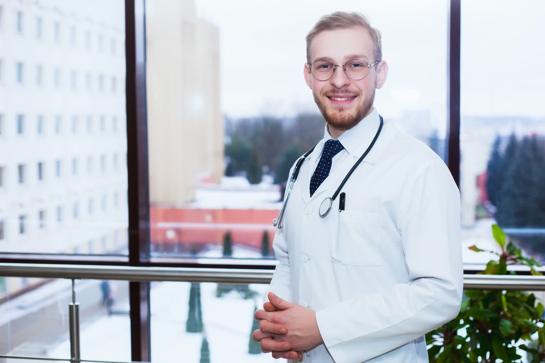 A hospital doctor standing at a corridor window overlooking the campus